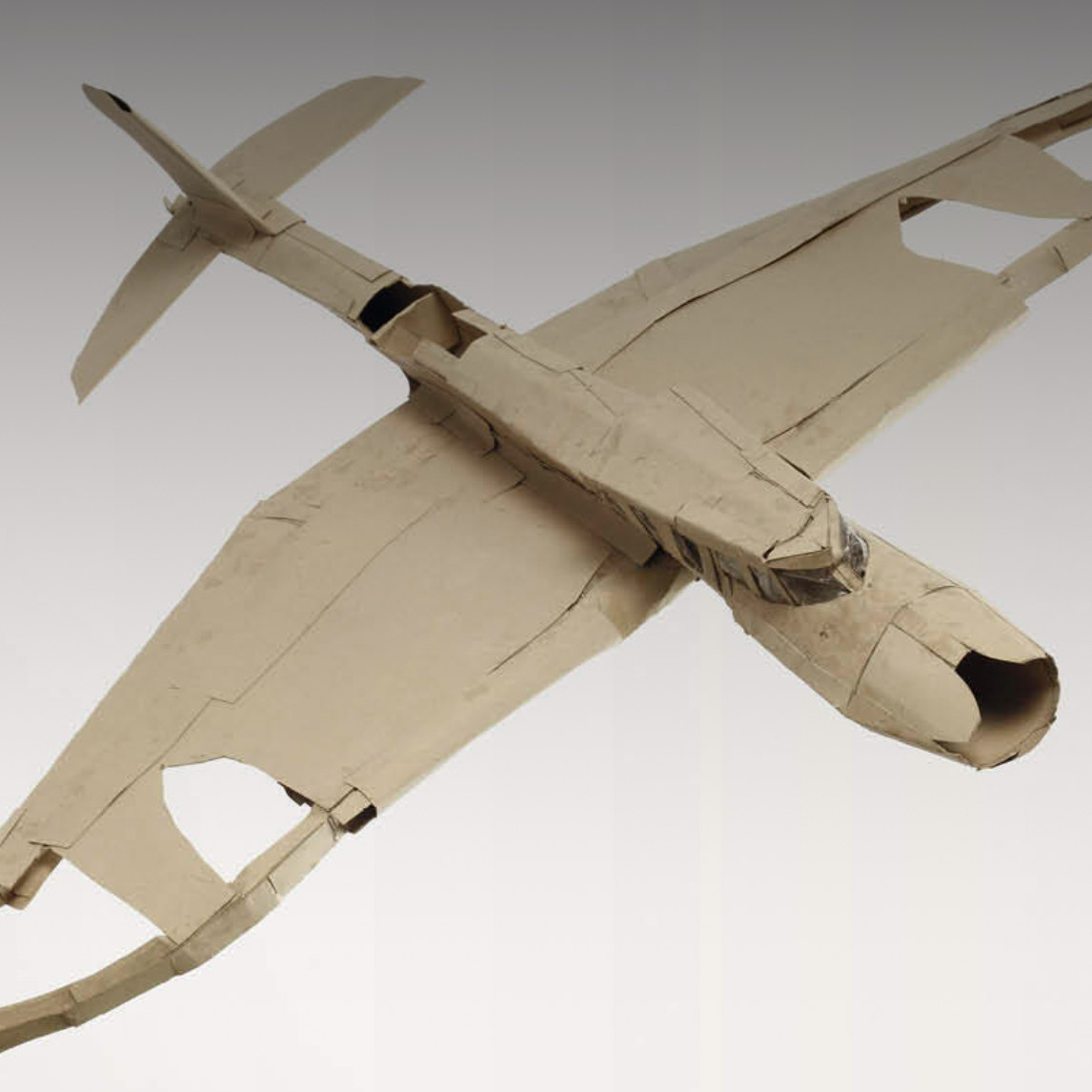 Ein Modellflugzeug aus Pappe mit ausgebreiteten Flügeln. Die Oberfläche wirkt uneben, die Kanten sind geknickt und geklebt.  Ein Modellflugzeug aus Pappe mit ausgebreiteten Flügeln. Die Oberfläche wirkt uneben, die Kanten sind geknickt und geklebt.